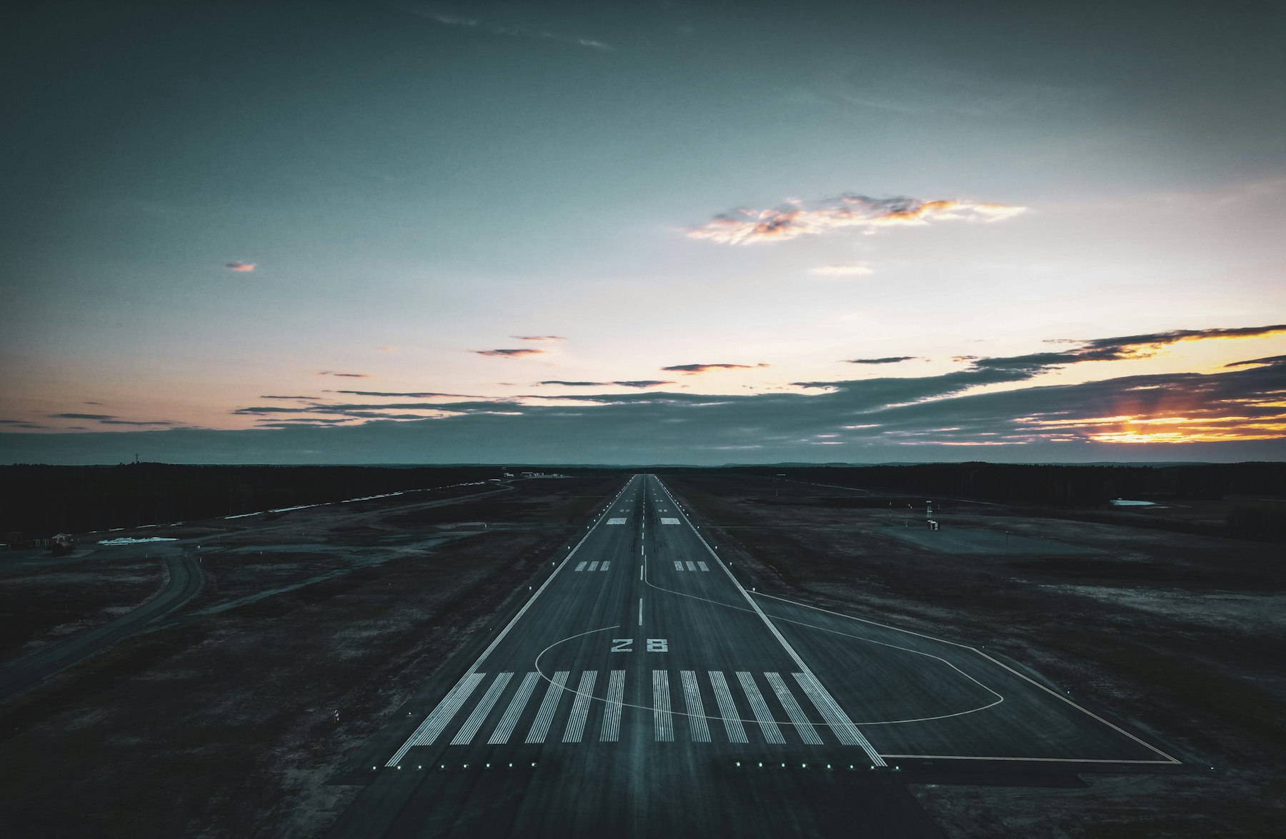 An airport runway at dusk, lights leading toward the horizon.